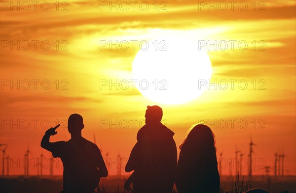 People on Berlin's Drachenberg at sunset. A wind farm near Nauen in Brandenburg can be seen in the