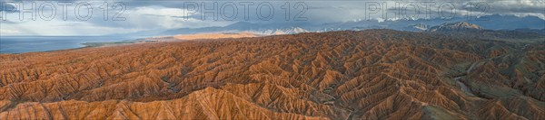 Panorama, landscape of eroded hills, badlands at sunset, behind mountain peaks of the Tian Shan