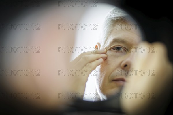 Symbolic photo on the subject of eye wrinkles. A man looks at his eye wrinkles in the mirror.