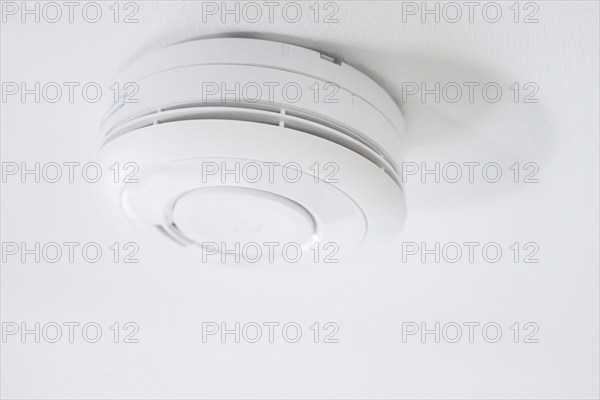 Symbolic photo on the subject of smoke alarms. A smoke detector hanging from the ceiling in a flat.