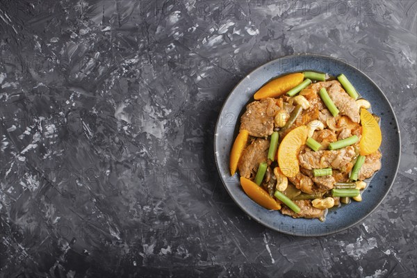 Fried pork with peaches, cashew and green beans on a black concrete background. Top view, copy