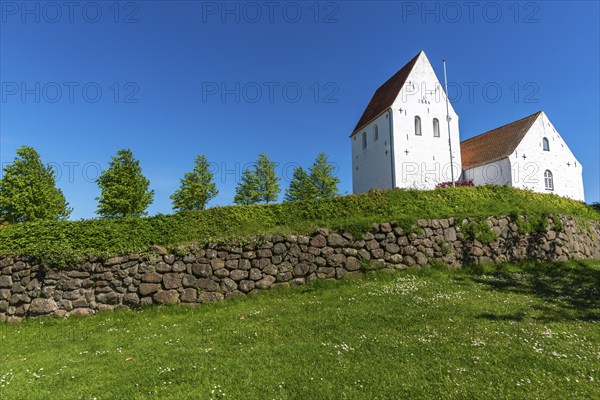 Ulbølle Kirke, whitewashed church on a hill, red roof tiles, group of trees, wall with boulders,