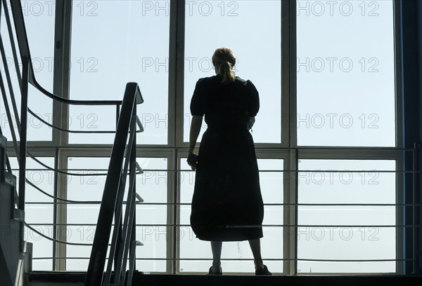 A woman stands at a window in a stairwell, Berlin, 26/06/2024, Berlin, Berlin, Germany, Europe