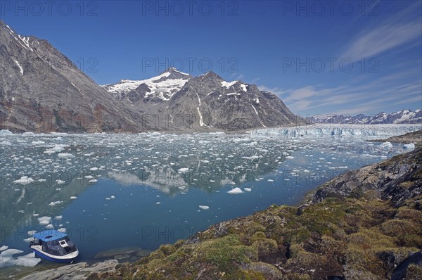A small boat moored on a clear fjord in front of an impressive mountain and glacier landscape, Knud