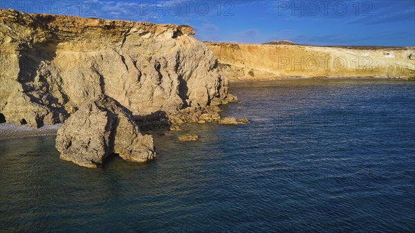 Dramatic cliff landscape with calm blue water, drone shot, evening light, Araki Beach, southwest