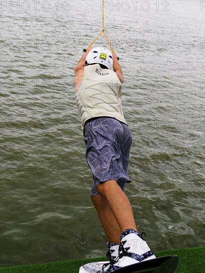 Young man with wakeboard at the jump start, water sports in the wakepark