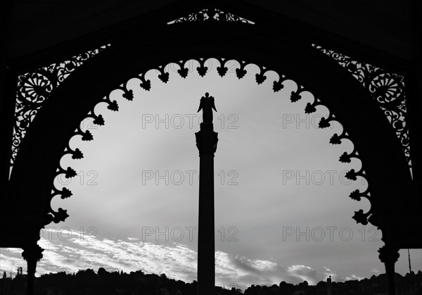 A statue stands on a pillar under a richly decorated archway