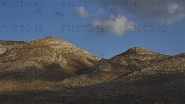 Rocky hills under a blue sky with scattered clouds and shadows, Kassos Island, neighbouring island