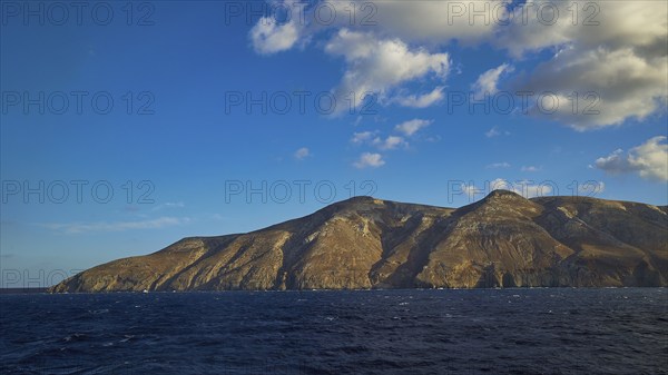 Rocky coast of an island under blue sky and light clouds, Kassos Island, neighbouring island