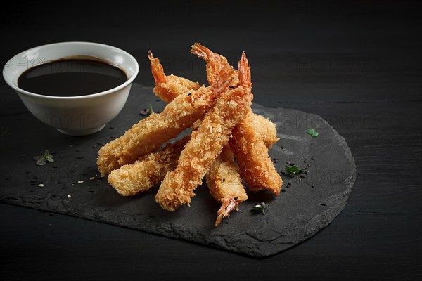 Shrimp in tempura, deep-fried, on black slate, with soy sauce, horizontal, no people