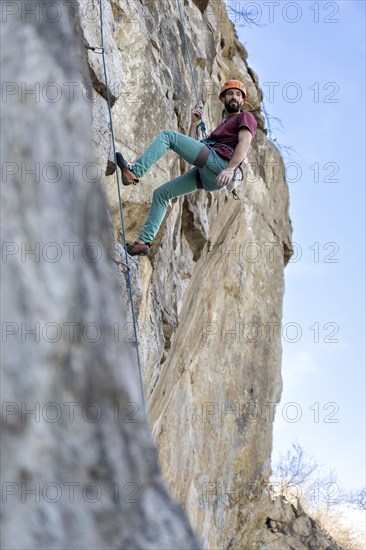 A young man climbs a challenging cliff route, secured by a rope, showcasing strength and