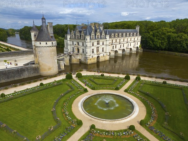 Castle and gardens with central fountain and geometric gardens by the river and under a cloudy sky,
