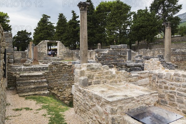 Old stone structures and columns plus tourists at ancient 3rd century Roman ruins of Salona near