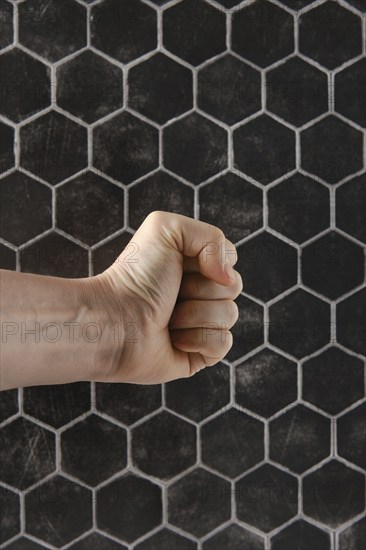 A strong fist is positioned in front of a textured hexagonal pattern, showcasing tension and