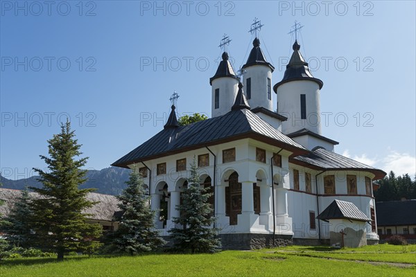 White orthodox church building with black roofs under a clear blue sky, Romanian Orthodox Monastery