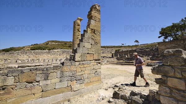 Man walking through a site with ancient stone ruins under a clear sky, Kamiros, Archaeological