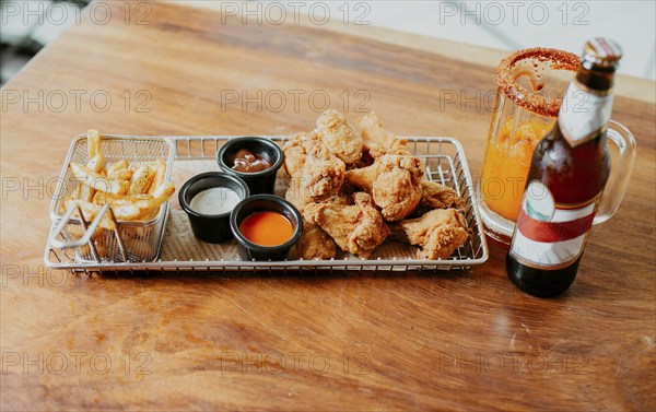 Top view of spicy wings with fries and michelada accompanied with beer served on wooden table