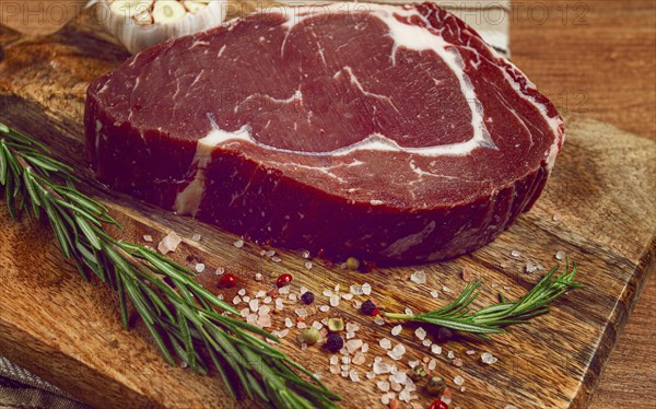Raw steak, beef steak, rib eye steak, on a cutting board, freshly frozen, with spices and herbs, on