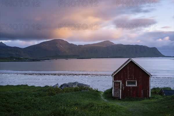 A red wooden hut on the sandy beach of Ramberg (Rambergstranda), with the sea behind it. At night