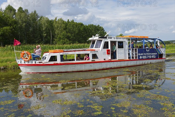 A white and red passenger boat sails along a quiet canal, surrounded by green nature, Zefir ship,