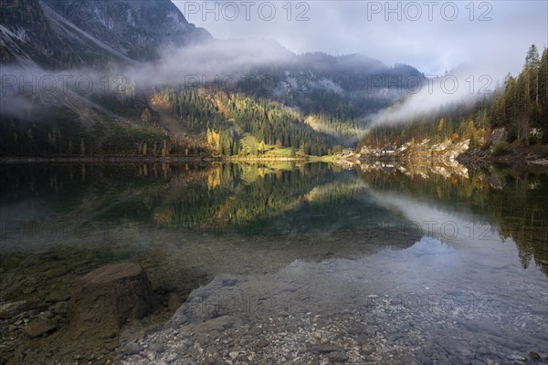 The Vordere Gosausee in autumn with a view of the Gasthof Gosausee. Sun and clouds. Overcast.