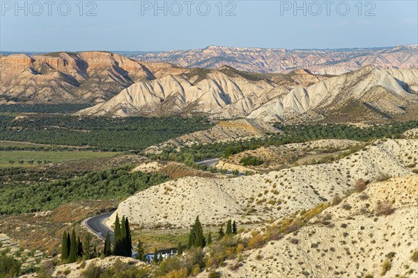 Wide desert landscape with rocky hills and serpentine road under a blue sky, Dehesas de Guadix,