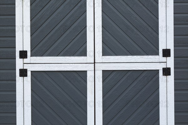 Individual small square doors on storage shed cladded with grey and white trim canexel wood