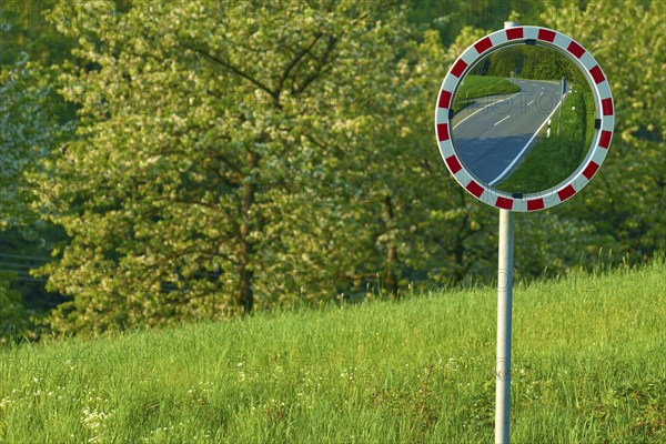 Traffic mirror reflecting a road, trees and meadow in the background, Odenwald, Hesse, Germany,