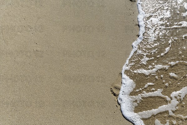 Gentle wave on the shore blurs footprint in the sand, Simos beach, text free space, symbolic photo,