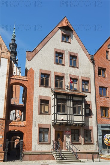 A historic half-timbered building with red brick elements and a high tower in the background under