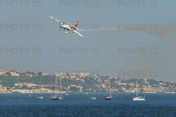 Stunt aerobatic plane Edge 540 performing stunts in blue sky at Oeiras Air Show above yacht boats