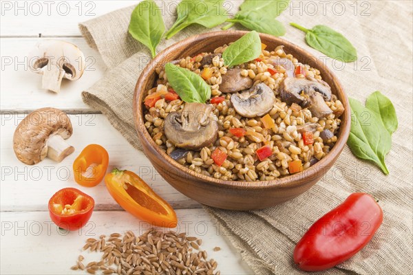 Spelt (dinkel wheat) porridge with vegetables and mushrooms in wooden bowl on a white wooden