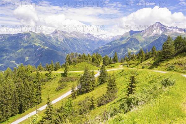 A picturesque landscape with green mountains, hiking trails and trees under a blue sky with clouds,