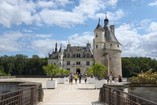 Tourists visiting a historic castle with a striking tower and blue sky in the background, Château