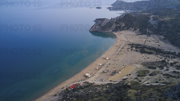Aerial view of a secluded sandy beach landscape with clear blue water and a few huts, Tsambika