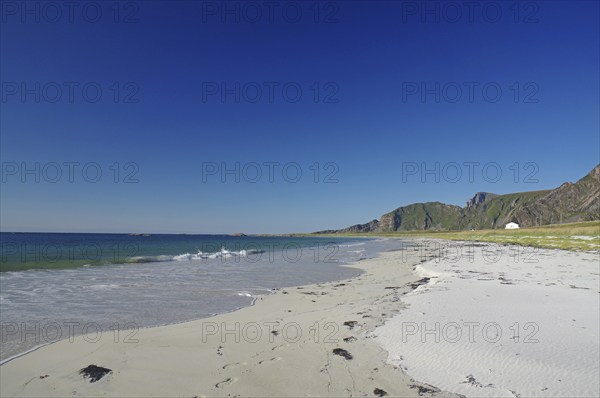 Beautiful beach with clear blue sky, gentle waves and mountains in the background, Bleik,