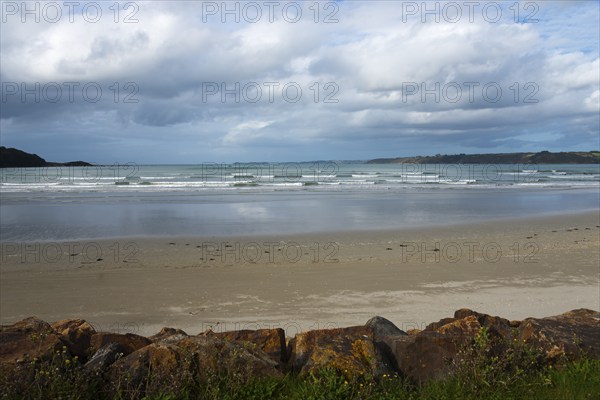 Lonely beach with gentle waves, covered by a cloudy sky and surrounded by rocks, Plage Saint