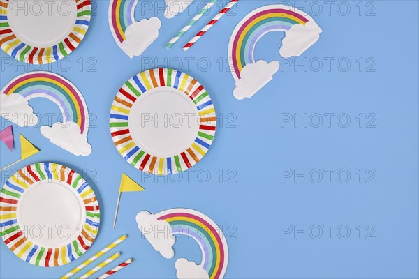 Party flat lay with colorful plates, rainbow napkins and drinking straws on blue background with