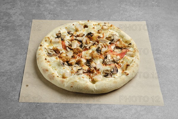 Pizza with chicken breast and champignon mushrooms on parchment paper
