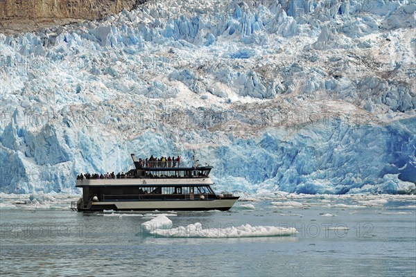 Passenger boat in front of the front of a glacier calving into the sea shimmering bluish, Tracy Arm