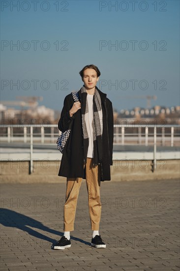 Full length portrait of young man in old wool coat, scarf and short trousers with backpack outdoor