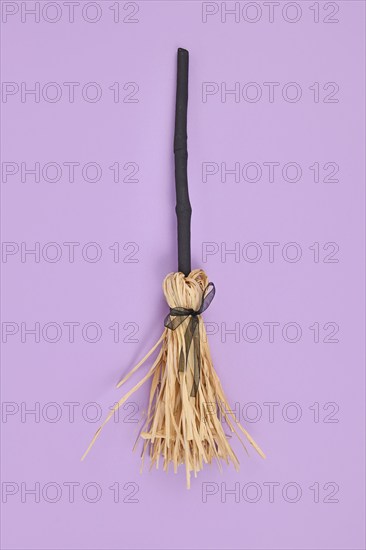 Witch broom with black twig and straw bristles on violet background