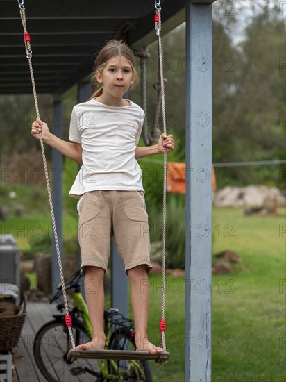 Boy swinging standing on children's swing at shed, Germany, Europe
