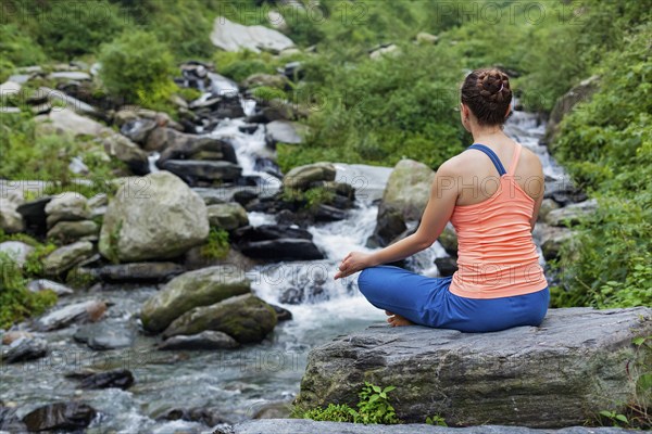 Woman in Hatha yoga asana Padmasana outdoors at tropical waterfall