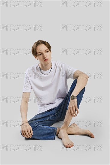 Young barefoot man sits on the floor in studio in t-shirt and jean