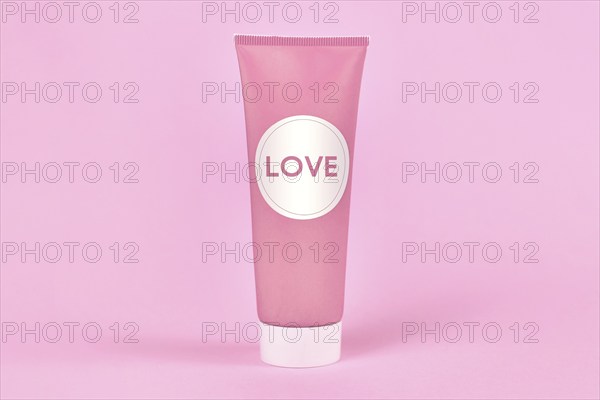Love concept with cream tube with made up label saying LOVE on pink background