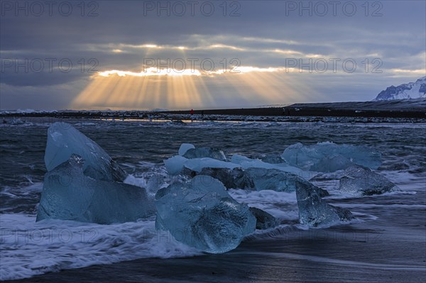 Waves breaking on icebergs on the black beach of Breidamerkursandur, sunset, near Jökullsarlon,