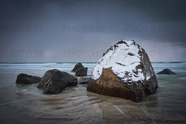 Rocks covered with snow on Norwegian sea beach in fjord in stormy weather with clouds. Skagsanden