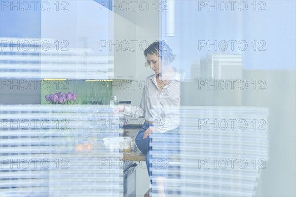 View through the window into the kitchen with beautiful woman inside sitting on teble top