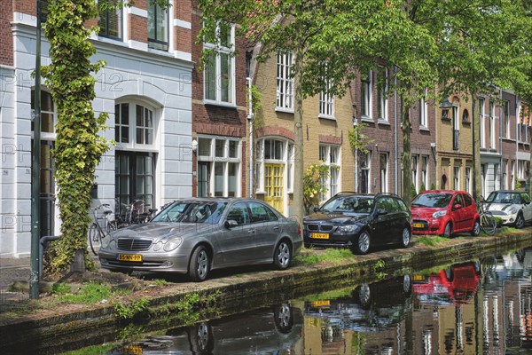 Delft, Netherlands, May 12, 2017: Cars and bicycles parked on canal embankment in street of Delft